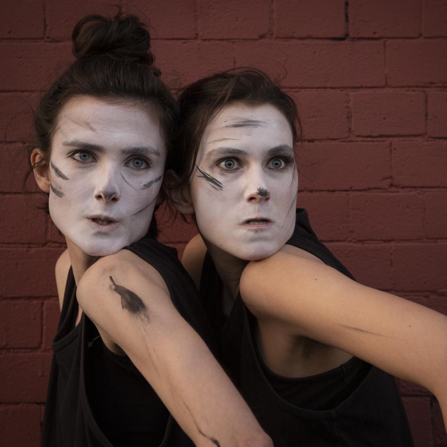 Two women posing and looking beyond camera, faces smeared with white paint and black lines  