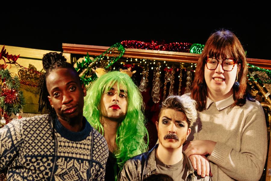 The cast members of A They In A Manger wearing Christmassy outfits and posing inside a festive-decorated wardrobe.