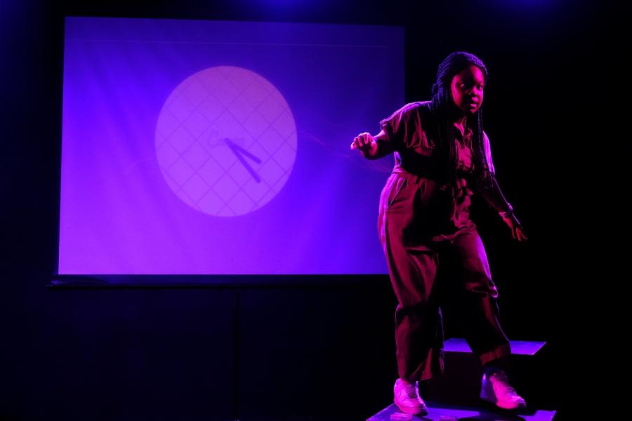 Corrine Walker: A black woman with hair in black braids stands on one leg on a black box. Behind her is a screen with a clock on it. Fuse: Dancer, Lucy, is kneeling on the floor with her arm extended upwards and leg bent behind her. Golden circles shine b