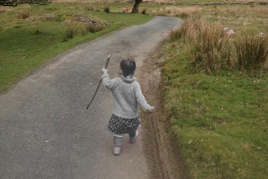 A black-and-white little girl walks with a stick along a color country road landscape.