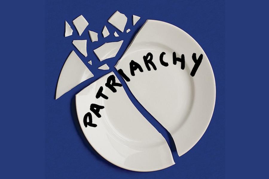 The bird's eye view of a broken plate with the word Patriarchy written on it in bold black ink. The background of the image is a deep blue. 