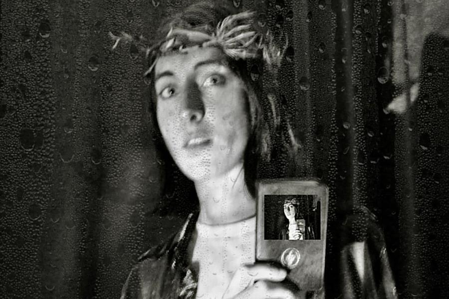 Black and white photo of performer wearing crown of thorns, holding a pocket bible. Everything overlayed with raindrops. 
