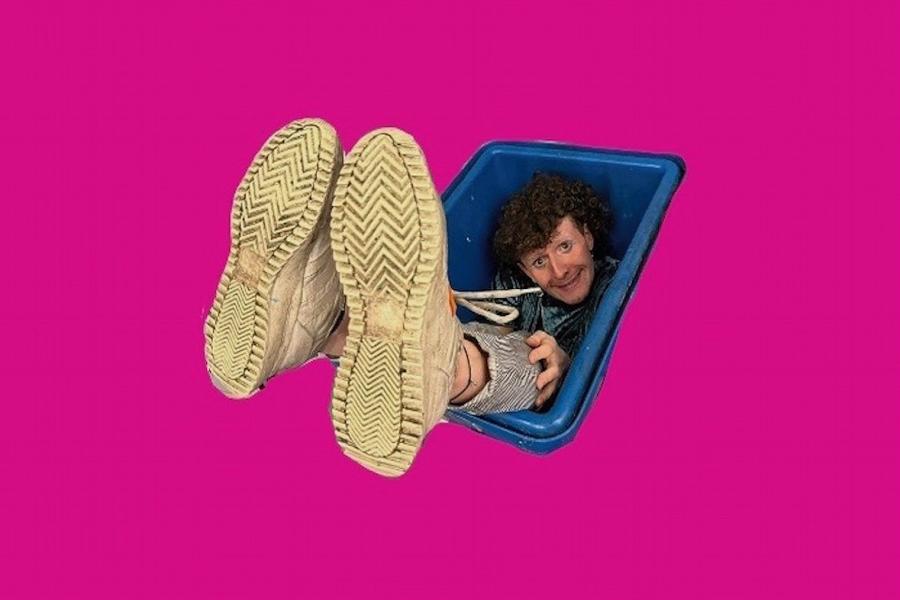 A crop out of Fraser in a blue bucket with his feet sticking out. They look really big because they're in the foreground. Against a hot pink background. 