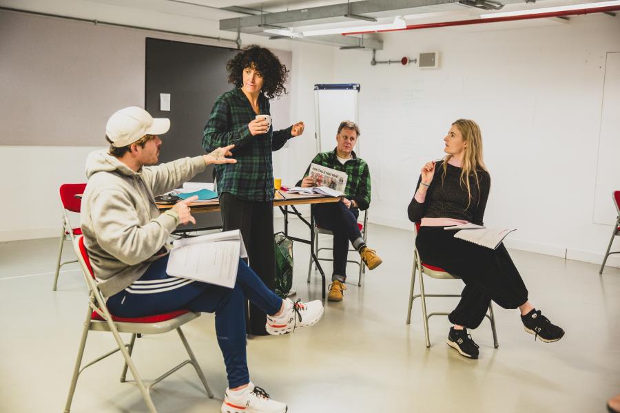 Three cast members sit while one stands, all engaged in rehearsal with scripts. Pictured: James Boyle (Jake), Anna Seymour (Rita), Louis Neethling (Mike), and Erin Hutching (Jane).