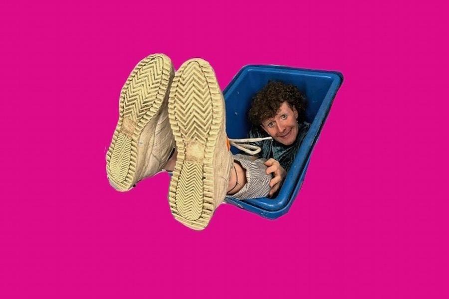 A crop out of Fraser in A blue bucket with his feet sticking out. His feet appear oversized as they're in the foreground. The image is against a hot pink background.