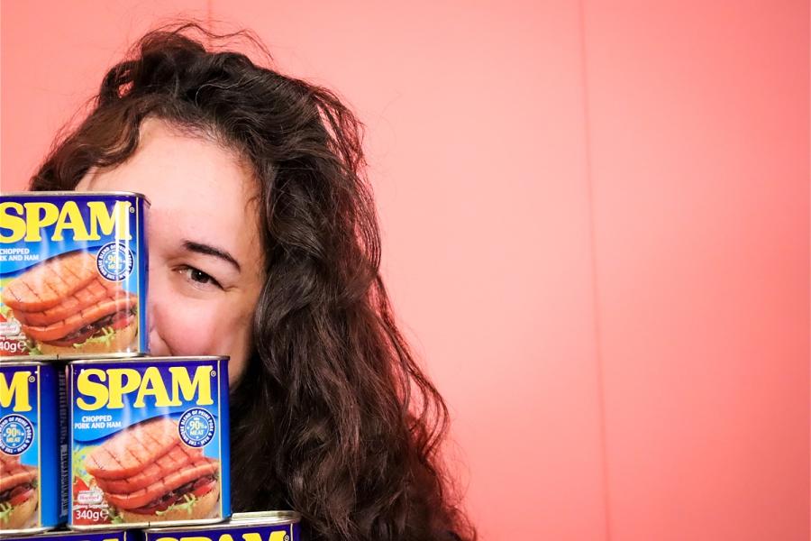Sierra peers and smiles with one eye from behind a stack of Spam cans.
