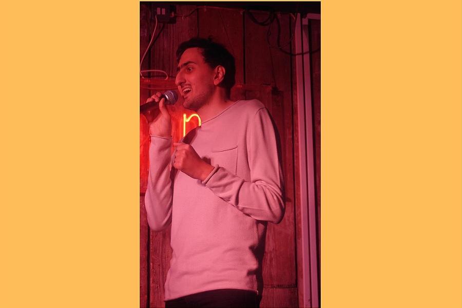 An image of Aarian on stage holding a microphone.  He is a clean shaven Middle Eastern man with thick black hair.