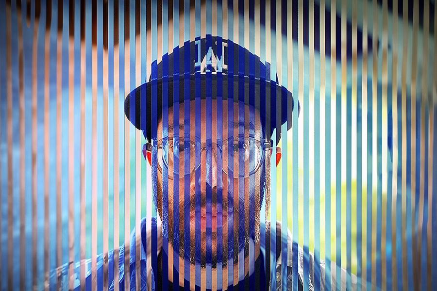 An image of a man with glasses, a beard and a baseball gap that has been cut up into vertical slices and reflected and glitched. It seems to suggest a man at conflict with himself who has been cut into pieces and seeks to put them back together.