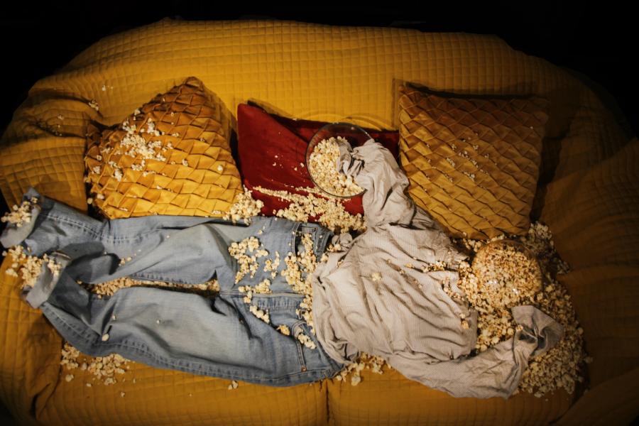 Clothing (blue jeans and a stripy top) filled with popcorn, lying on a sofa yellow sofa. You can see there was once a person that has now disintegrated into nothingness.  