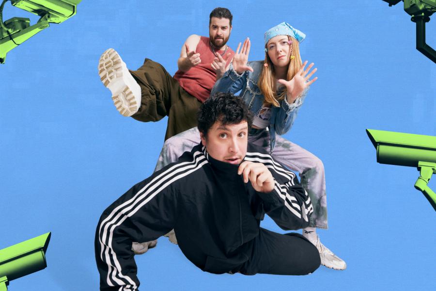 A woman wearing black Adidas trousers and a purple jumper and two men wearing black Adidas tracksuits sit on a blue floor facing the camera. Behind the group, CCTV cameras are positioned against a digital glitch screen wallpaper.