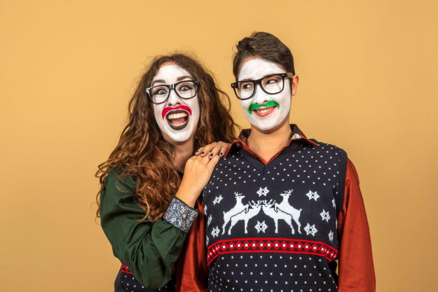 Two performers in xmas jumpers and boxers with white facepaint and moustaches painted on doing what can only be described as Christmas shennanigans.