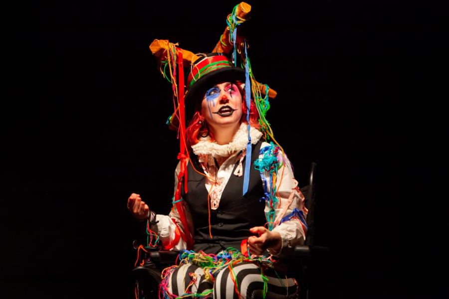 A person dressed up as an eccentric clown looks upwards towards the right. 