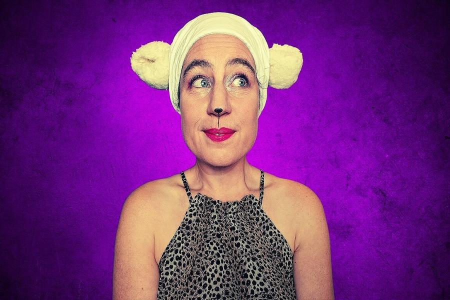 A caucasian woman in a leopard print top looks to the side. She has DIY sheep ears and a painted sheep's nose