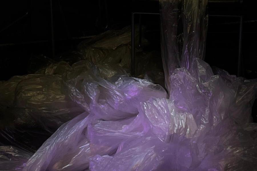 Clear plastic sheets bunched together dumped on the floor and hanging from above. Lit in purple with a dark background