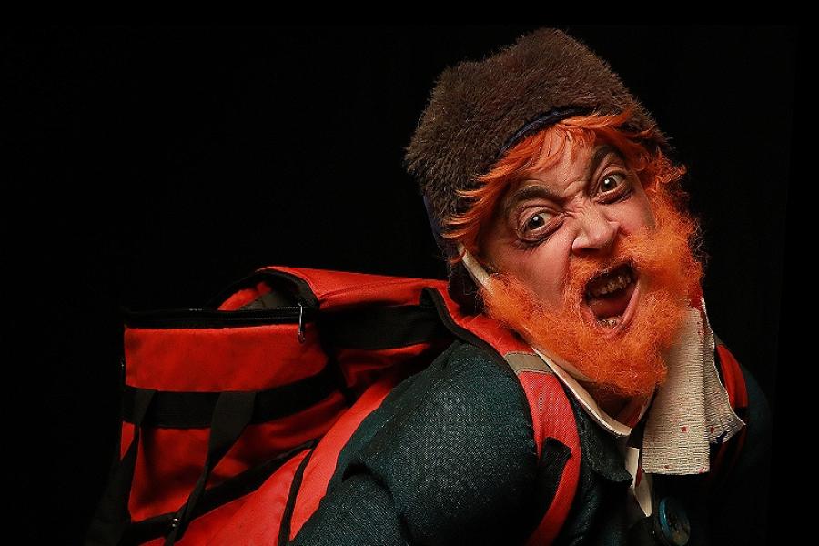 An man with orange hair, a scraggly beard, a bandage around his head and a food delivery backpack makes a distorted face toward the camera.