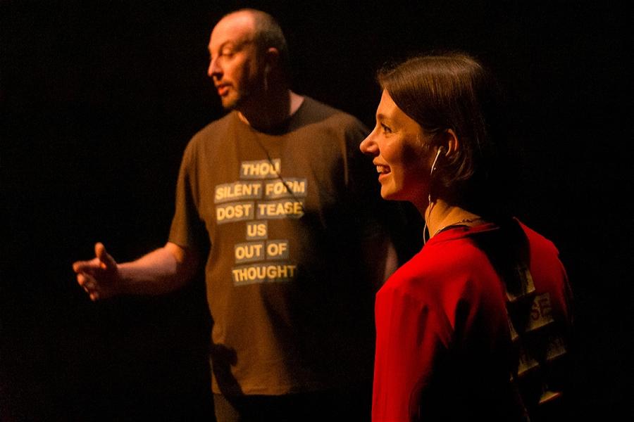 A woman and a man smile at the audience. On the man's t-shirt are the words 'Thou silent form dost tease us out of thought'.