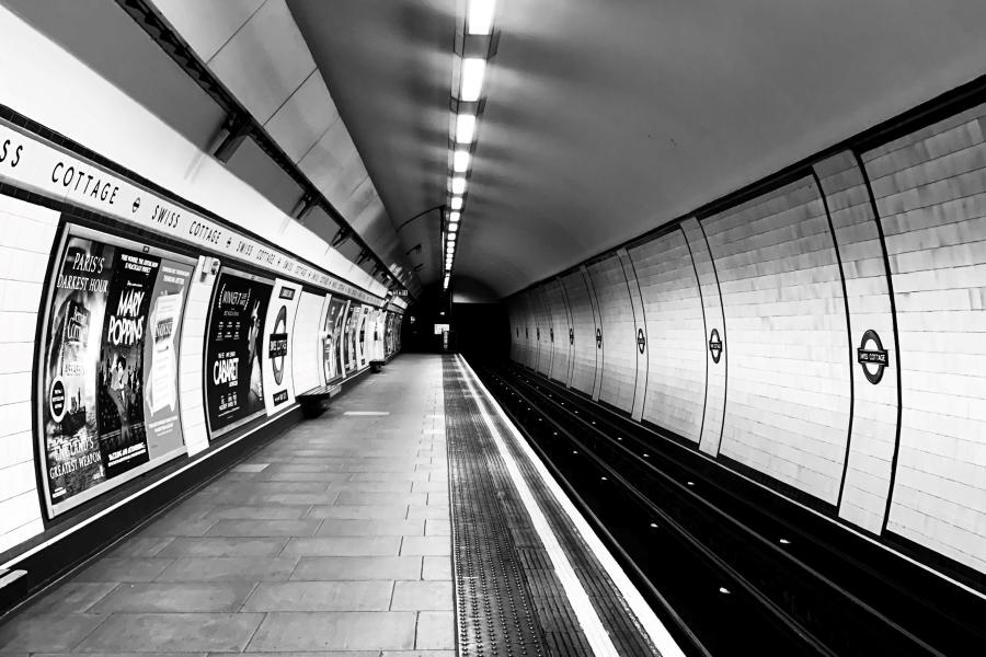 A black-and-white image at a tube station showing a bare platform, rail tracks and overhead lights