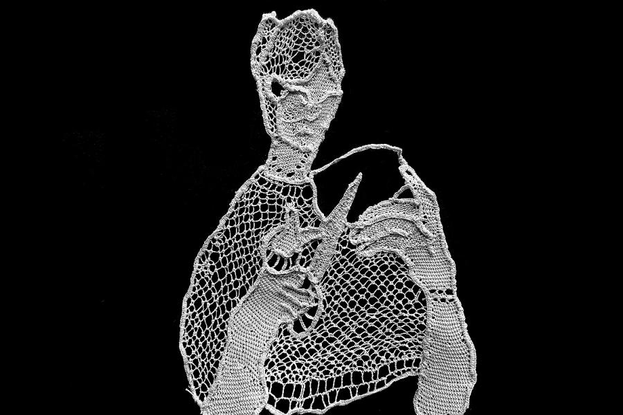 White needle point tapestry against a black background of a woman holding a pair of scissors. The scissors are open and pointed towards her as if she is about to cut one of her threads.