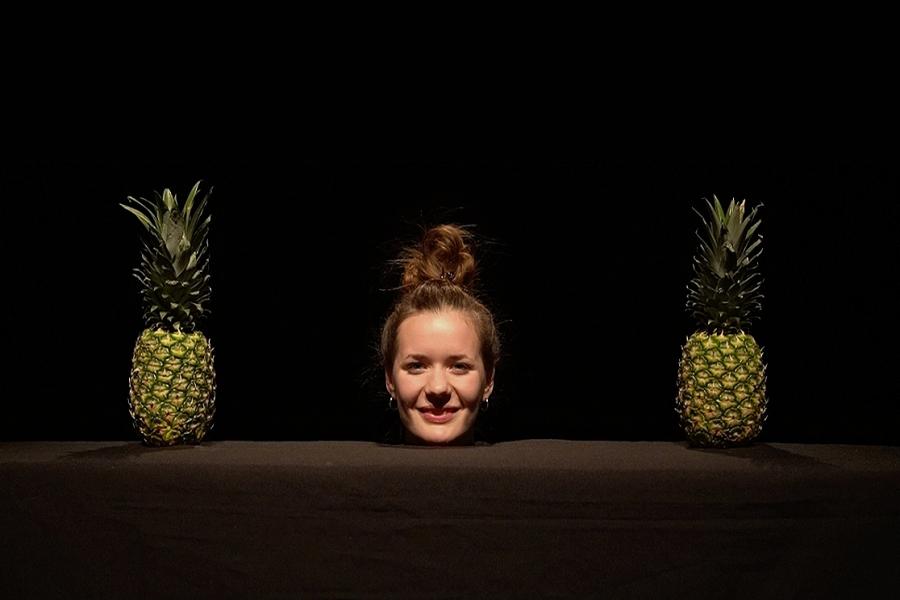 A womens face with her hait up in between two pineapples.