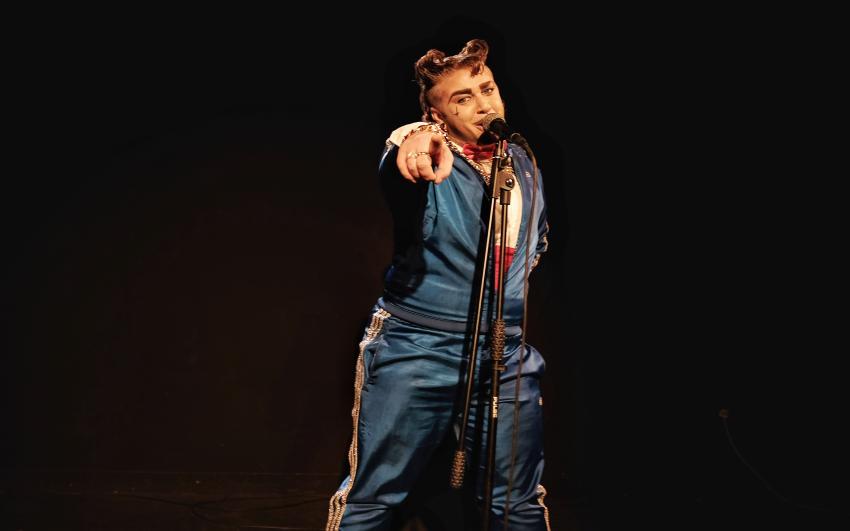 Photograph of a performer on stage at CPT in a blue tracksuit pointing directly at the camera