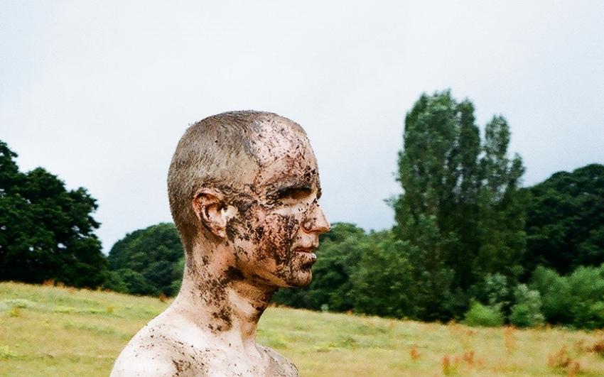 Actor Alistair Hall poses as character Jimbo, the central character in DECLAN. He is muddied and gazing out into a field. 