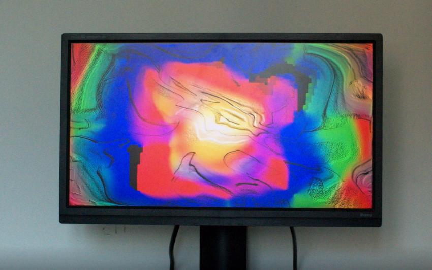 A computer monitor, showing a psychedelic blend of multiple coloured pixels on its screen