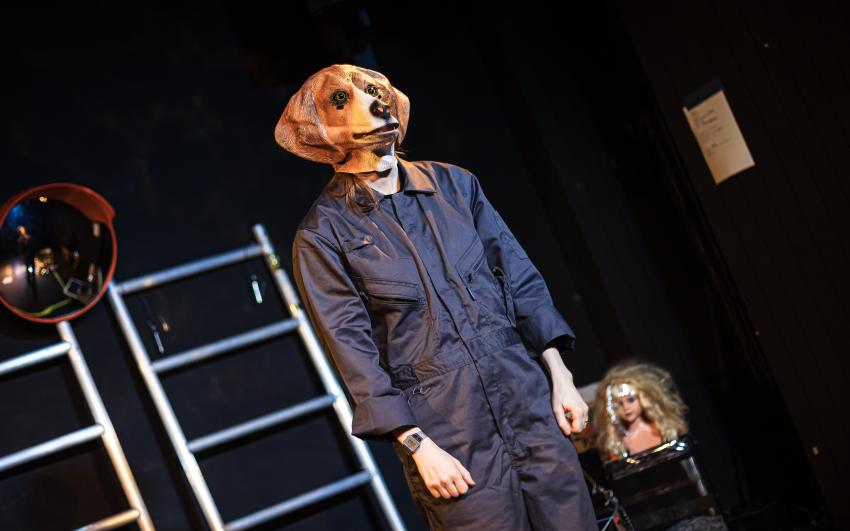 Photo of a performer in a blue boiler suit wearing a dog head mask