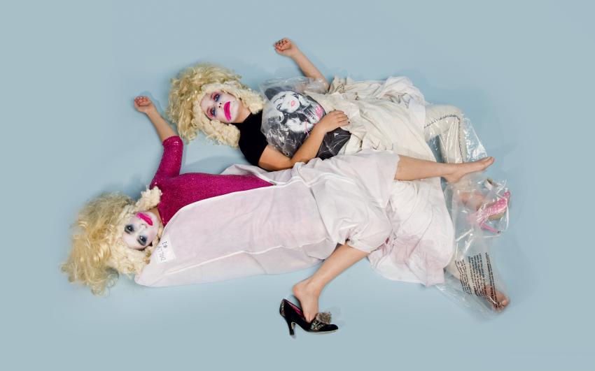 Two performers dressed up with smeared face paint, blonde wigs, laying on the floor
