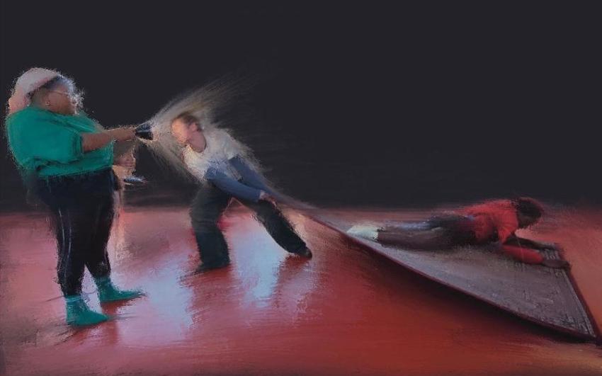 A blurry image of three people. One holding a torch, a second lying down on a carpet and a third pulling the carpet along